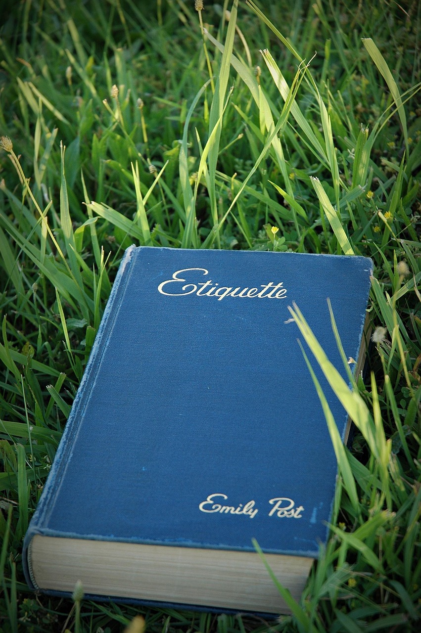 A blue book titled 'Etiquette' by Emily Post resting on green grass.